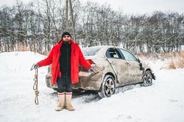 Çekici ipi olan bir adam ellerini kaldırır, kışın yol kenarında kaza yapmış bir arabanın yanına..