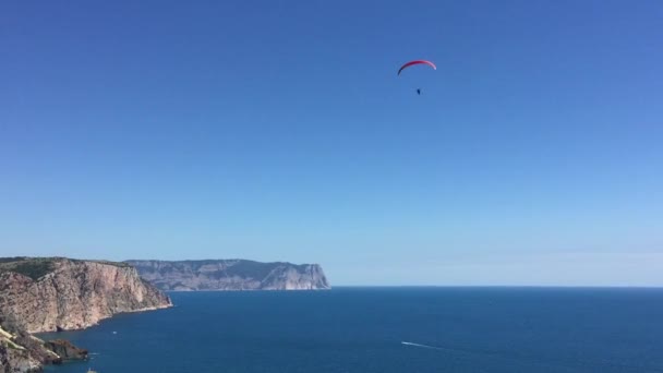 パラシュートの男が山の海岸に沿って海を滑り降りる — ストック動画