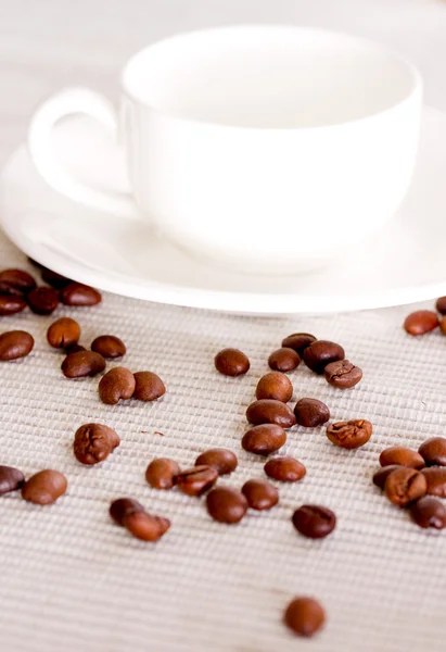 Granos de café y taza de porcelana blanca en el fondo —  Fotos de Stock