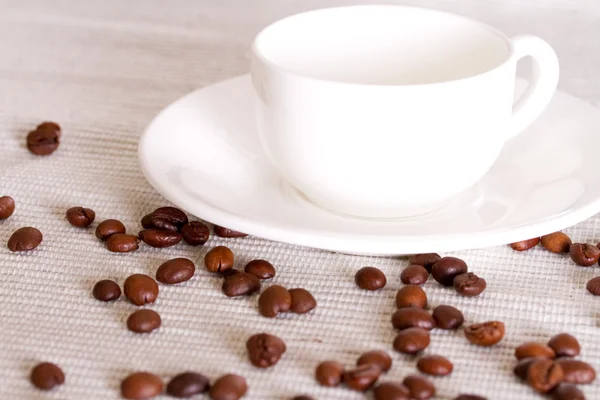 Grãos de café e xícara de porcelana branca no fundo — Fotografia de Stock