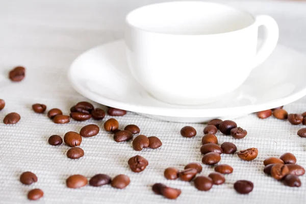 Grãos de café e xícara de porcelana branca no fundo — Fotografia de Stock