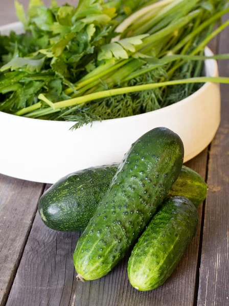 Cucumbers on old wooden boards and a plate with parsley, dill an — Stock Photo, Image