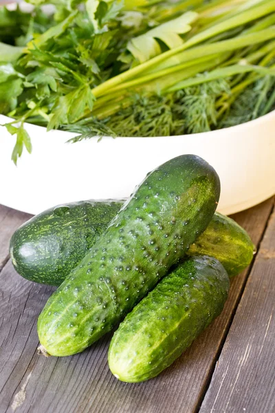 Cucumbers on old wooden boards and a plate with parsley, dill an — Stock Photo, Image