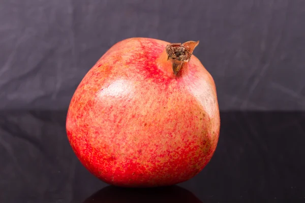 Ripe pomegranate on a black shiny surface — Stock Photo, Image