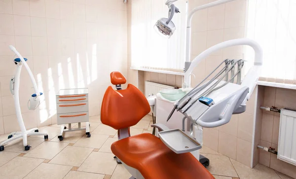 Interior of new modern dental clinic office room with chair in red orange and white colors. Dentistry, stomatology, medicine medical equipment concept in teeth cabinet