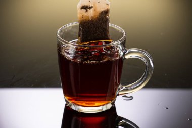 Şeffaf bir fincandaki sosis poşetinden siyah çay demle. Arkaplanda yansıması olsun.