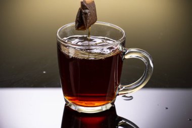 Şeffaf bir fincandaki sosis poşetinden siyah çay demle. Arkaplanda yansıması olsun.