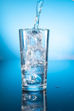 Şeffaf bardaktaki temiz buzlu su mavi gradyan arkaplanda yansıyor.