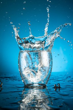 Splash in a glass of water from a falling piece of ice on a blue background clipart