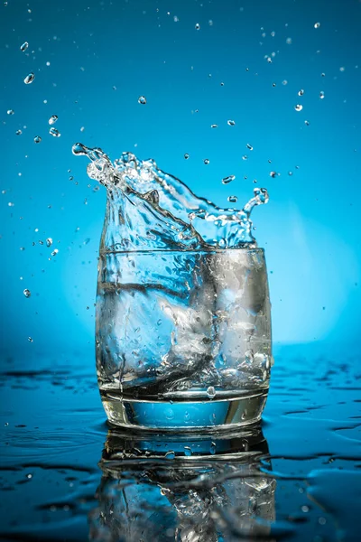 Выплеск Стакане Воды Падающего Куска Льда Голубом Фоне — стоковое фото