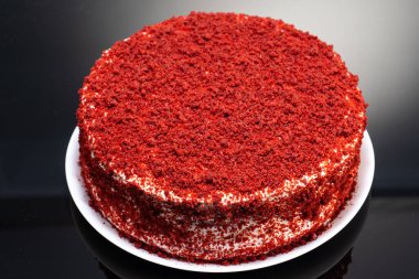 Kırmızı kadife pasta, beyaz kremalı ve beyaz bir tabakta yansımalı kırmızı kırıntılar.