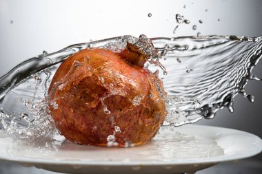 Beyaz tabakta tam nar meyvesi ve su sıçraması.