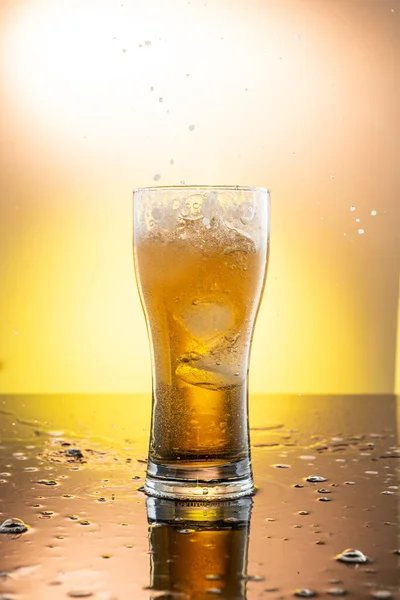 Šplouchnutí Kusu Ledu Sklenici Pivem Žlutém Pozadí — Stock fotografie