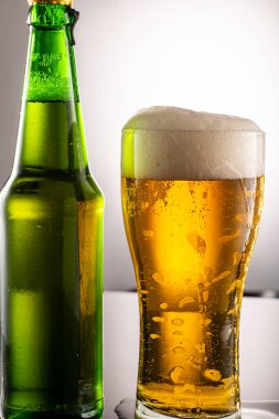 Bira bardağı, köpük ve yanında bira olan yeşil şeffaf şişe.