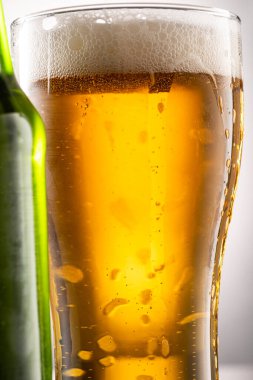 Bira bardağı, köpük ve yanında bira olan yeşil şeffaf şişe.