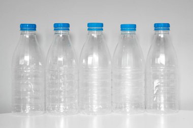 Geri dönüşüm için mavi başlıklı plastik şişeler gri bir arkaplanda beyaz bir masada duruyor. Plastik ve ekoloji geri dönüşüm kavramı. Plastik atık. Doğa saçmalığını durdur