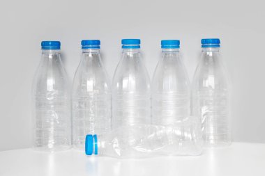 Geri dönüşüm için mavi başlıklı plastik şişeler gri bir arkaplanda beyaz bir masada duruyor. Plastik ve ekoloji geri dönüşüm kavramı. Plastik atık. Doğa saçmalığını durdur