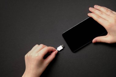 Kız siyah arka planda akıllı telefondan para alıyor. Yukarıdan bak. Flatlay. Telefon şarj. Cep telefonu şarjını USB tip C (USB-C) ile kapat. USB tip C kablo şarj cihazı ve telefonun port numarası.