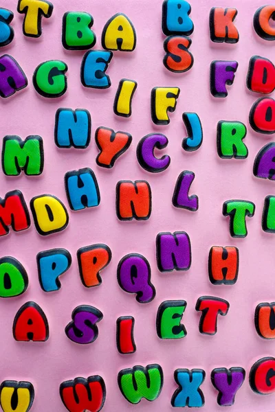 The multi-colored letters of the English alphabet are scattered on a pink background. Learning the alphabet. The concept of education in kindergarten and school. Alphabet for stores, sales, websites.
