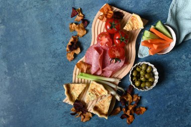 Bir piknik tabağı domatesli kiş zeytinli salata ve sebzeli bir masanın üstünde hazırlanır.