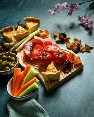 Bir piknik tabağı domatesli kiş zeytinli salata ve sebzeli bir masanın üstünde hazırlanır.