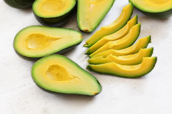 Avocadostücke Und Hälften Mit Leuchtend Gelbem Fruchtfleisch Auf Weißem Steinbrett — Stockfoto