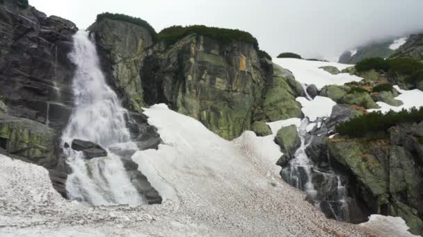 Vodopád Skok na oblačném jarním dni, voda padá do špinavého tání sněhu přes skály