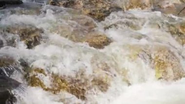 Kayaların üzerinden akan su, bahar nehrinde beyaz dalgalar oluşturur. Yakın çekim ayrıntıları, yavaş çekim görüntüleri.