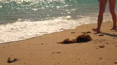 Yüzen genç bir kadın, ıslak kumsalda çıplak ayakla yürüyor, bacaklarında detay var.