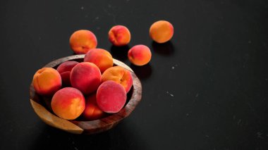 Kayısılar küçük ahşap kasede, bazıları siyah masaya dökülmüş, sağ tarafta yazı için yer var.