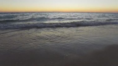 Gün batımından hemen sonra kumsalları yıkayan küçük dalgalarla sakin okyanus.