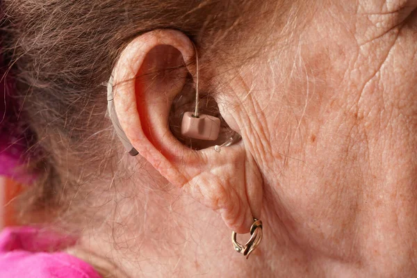 Hearing aid device in senior woman ear - closeup detail