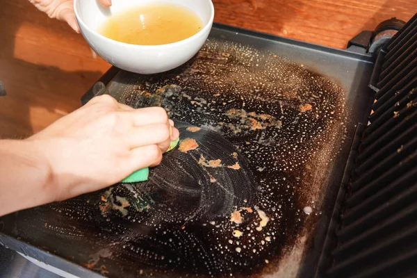 Cleaning electric grill dirty plate with soaped sponge, detail on woman hand