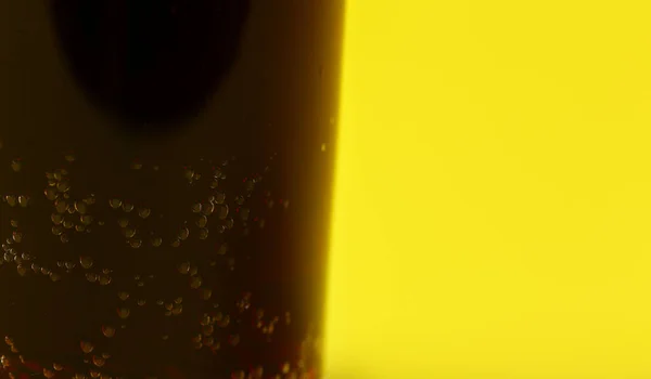 Small bubbles in dark fizzy drink, closeup detail with yellow background