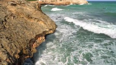 Kayalık kıyılara çarpan küçük dalgalar, suda yüzen bir grup tanınmayan sörfçü, arka planda dalgaların oluşmasını bekliyorlar.