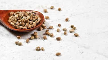 Soyulmamış kenevir - Kenevir sativası - beyaz taş masa üzerindeki küçük koyu tahta kaşıkta.