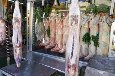 Akabe, Ürdün - 17 Ocak 2020: Çiğ et - tüm hayvan gövdeleri plastik folyoda asılı, dekorasyon için bazı yeşil yapraklar - yerel kasap dükkanında sergilenmektedir