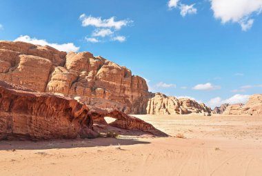 Wadi Rum Çölü 'nde küçük yay veya küçük kaya pencere oluşumu, parlak güneş kırmızı toz ve kayaların üzerinde parlıyor, mavi gökyüzü yukarıda.