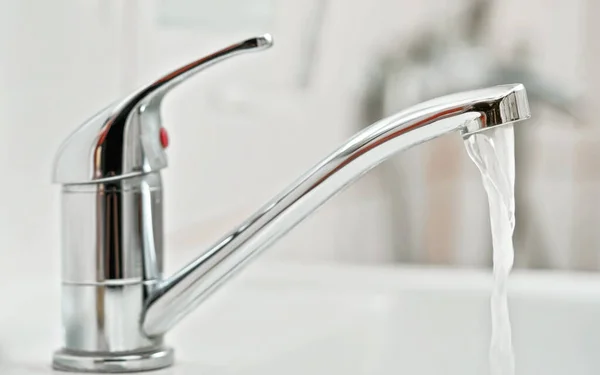 Tap water faucet, with running water, blurred bathroom background, view from side