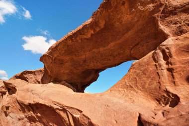 Wadi Rum Çölü 'nde küçük yay veya küçük kaya pencere oluşumu, parlak güneş kırmızı toz ve kayaların üzerinde parlıyor, mavi gökyüzü yukarıda.