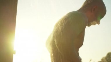 Sahilde sabah duşu alan genç adam arka planda parlıyor.