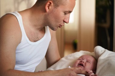 Çelik yelek giyen genç bir adam, küçük oğluyla oynuyor, sakinleşmeye çalışıyor, onu tutarken bağırıyor.