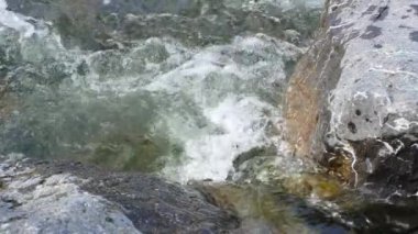 Bahar nehri suyu iki büyük kaya arasında akıyor, yakın çekim detayı, yavaş çekim videosu