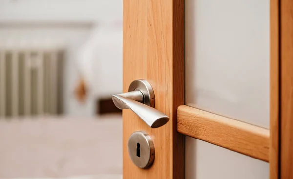 Opened modern wooden door into room, closeup detail on metal handle
