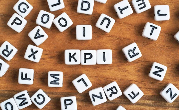 Small white and black bead cubes on wooden board, letters in middle spell KPI - Key Performance Indicators concept — Stock Photo, Image