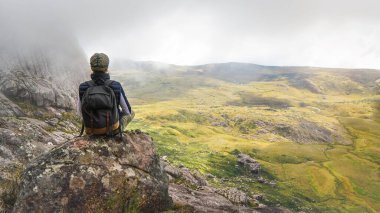 Spor elbiseli genç bir kadın, Andringitra Ulusal Parkı manzarasının tadını çıkarıyor. Büyük taşlar, kalabalık arka plan.