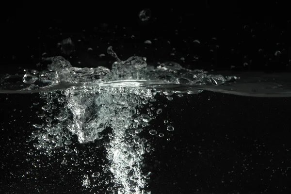 Water splashing as it\'s poured into aquarium tank, black background