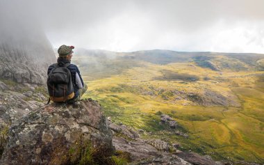 Spor elbiseli genç bir kadın, Andringitra Ulusal Parkı manzarasının tadını çıkarıyor. Büyük taşlar, kalabalık arka plan.
