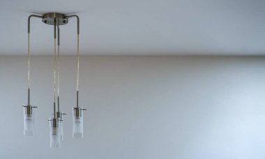 Modern metal ve cam lamba dört lamba asılı tavanı oluşturur, sağ tarafı boş.