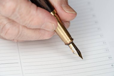 Son sınıf kadınının elindeki altın renkli dolmakalem boş günlük planlama sayfasına bir şeyler yazmak üzere.